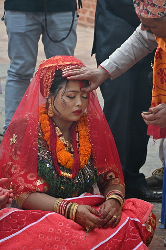 Kirtipur, Nepal - February 12, 2024 - A Newari Wedding starts with the ritual of, the groom side sending twelve areca nut in a huge silver bowl along with fruits, sweets, gold jewelry, clothes and other cosmetic accessories for the bride which are decorated and displayed in trays in an eye-catching way. The groom and the groom’s mother is absent in this ceremony whereas the bride’s mother starts the ceremony by worshipping lord Ganesh, lord of fire(Agni devta) and other god and goddesses. This ritual is usually performed four days before the wedding on the same day as the bride side’s reception party.