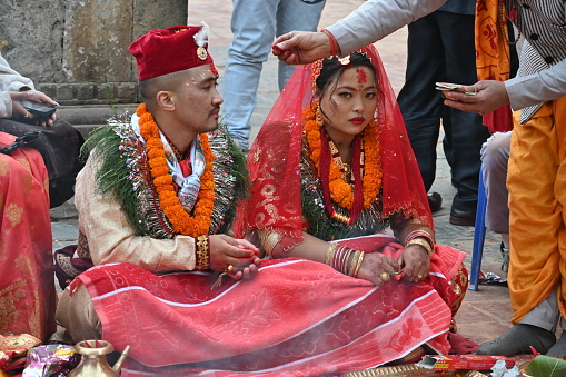 Kirtipur, Nepal - February 12, 2024 - A Newari Wedding starts with the ritual of, the groom side sending twelve areca nut in a huge silver bowl along with fruits, sweets, gold jewelry, clothes and other cosmetic accessories for the bride which are decorated and displayed in trays in an eye-catching way. The groom and the groom’s mother is absent in this ceremony whereas the bride’s mother starts the ceremony by worshipping lord Ganesh, lord of fire(Agni devta) and other god and goddesses. This ritual is usually performed four days before the wedding on the same day as the bride side’s reception party.