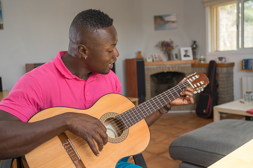 Young African American man e-learning to sing and play the guitar in his living room