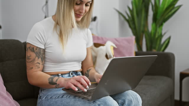 Tattooed woman using laptop with dog indoors