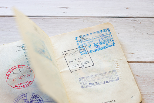 Old immigration stamps on passport. Immigration visas on an old Italian passport on a white  wooden background. Horizontal view