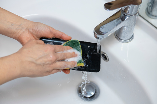 Woman washing smartphone under water in bathroom.