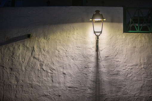 Street wall light illuminates a dark road and white wall 
casting shadows