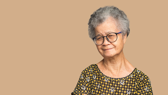 Portrait of a senior woman with short gray hair looking at the camera with a smile while standing on a brown background in the studio. Aged people and relaxation concept