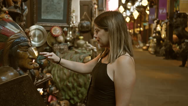 A woman explores traditional artifacts at souk madinat jumeirah in dubai, expressing curiosity and cultural immersion.