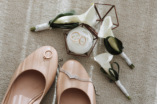 the bride's wedding shoes are beige, there are three calla flower boutonnieres and wedding rings in a glass box