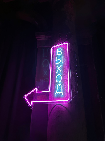 Vertical shot of Illuminated purple neon sign with an arrow and Cyrillic script, creating a moody and vibrant night scene, perfect for urban settings