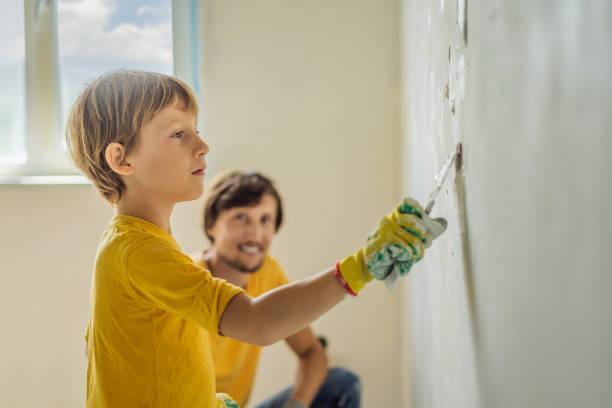 man with his son makes repairs at home, he teaches children to plaster the walls with a spatula in his hands - plaster plasterer work tool child foto e immagini stock