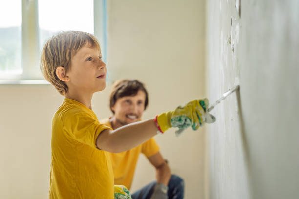 man with his son makes repairs at home, he teaches children to plaster the walls with a spatula in his hands - plaster plasterer work tool child foto e immagini stock