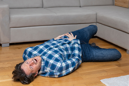 Mature man lying on floor with pain in his hip. Fallen down after fainting.