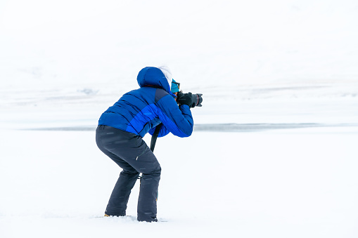 Adventurous photographer woman in winter in Iceland photographing on a frozen lake below zero