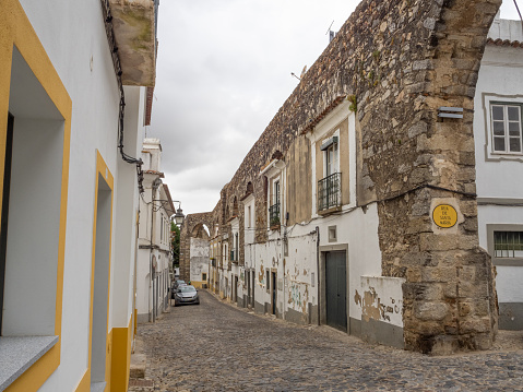 A cobbled street in the historic center of the city of Évora, with houses built within the arcades of the Água de Prata Aqueduct, in the Renaissance style. Portugal.