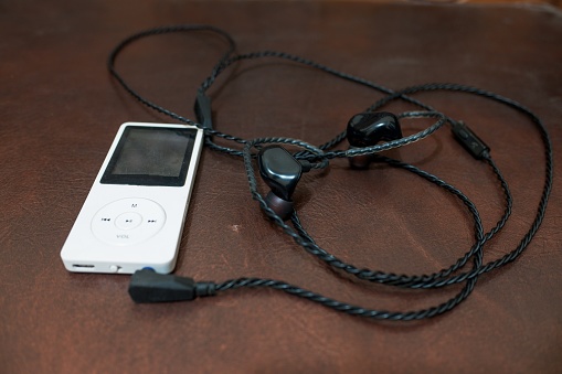 A white digital music player with a black headset on a brown background.