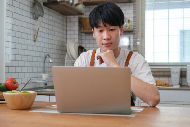 istock Smiling man having breakfast in modern kitchen at home and making video call via laptop. 2073247174