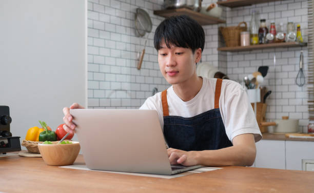 istock Smiling man having breakfast in modern kitchen at home and making video call via laptop. 2073247182