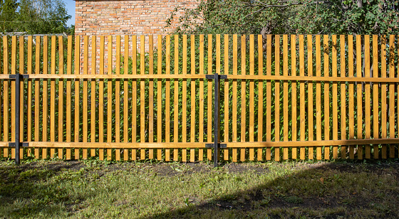 Close-up of a new wooden picket fence in the backyard of a country house, a sunny summer day.