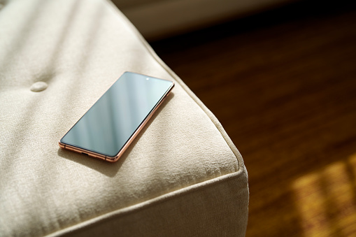 A black mobile phone is left on a sofa, with soft sunlight shining on it, high angle view