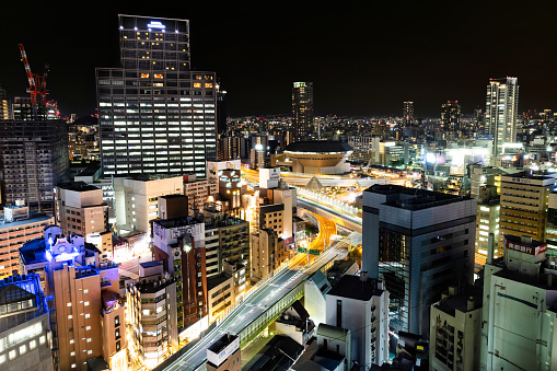 Osaka, Japan - October 11, 2023: A view of the Osaka skyline at night with buildings, roads, and bridges illuminated by lights.