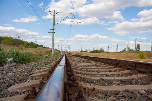 Close-up side view of steel railroad track outdoors in a sunny summer day. Blue sky with some white clouds. Soft focus. Copy space. Railway transportation theme.