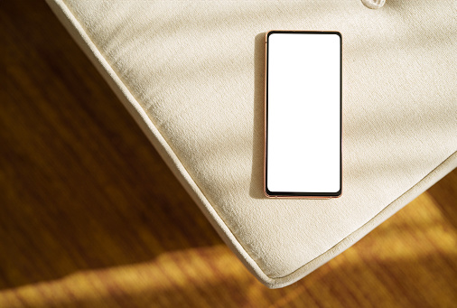 Directly above, a smartphone with a blank screen is placed at the edge of a sofa, suitable for mockup purposes