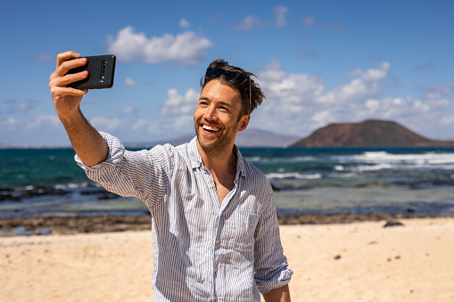 A young man rests on a sandy beach, takes a selfie for social networks