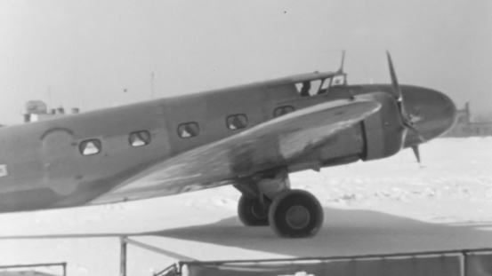 New York, USA, 1930s Winter: Side view of an early propeller passenger plane with pilot in cockpit, on a snow-covered runway, engines about to start, capturing the pioneering days of aviation.