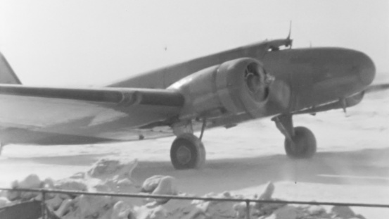 Close-up view of a 1930s airliner with engines running, waiting for passengers to board at a snowy New York airport. Captures the charm of air travel in a bygone era. Boeing 247 of United Air Lines