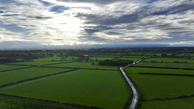 Aerial view of flat green land in Northern Ireland at sunset, Aerial view of green cultivated farmland with growing crops and distant village houses on bright summer evening, Aerial view of Northern Ireland sky cloudscape