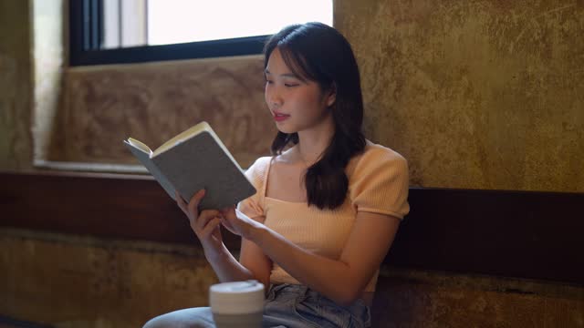 Asian woman working and reading at a cafÃ©, enjoying remote work. A relaxed and pressure-free atmosphere enhances her productivity