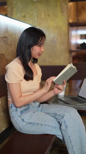 Asian woman working and reading at a cafÃ©, enjoying remote work. A relaxed and pressure-free atmosphere enhances her productivity