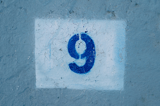 Number nine drawn on a scratched blue wall in a white rectangle. High quality photo