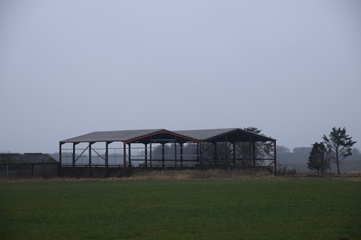 Outer farm buildings on a grey day with agricultural fields in the foreground.