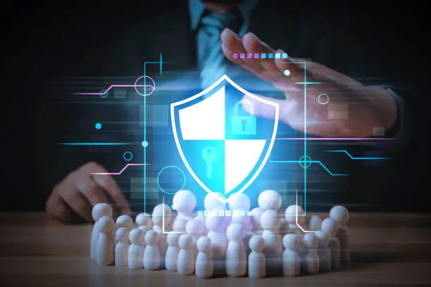 businessman is protecting a group of woodendoll or people with a shield. The shield is blue and has a key on it. Network security and data protection and safe your data concept, cybersecurity.
