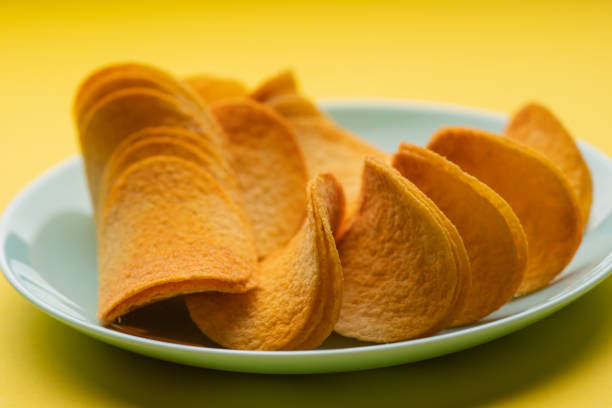 Crispy golden-brown potato chips on a blue plate against a bright yellow background stock photo