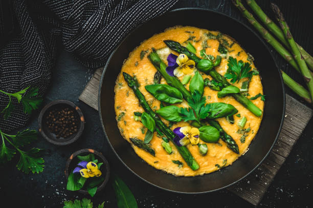 istock Omelette with green asparagus, basil and herbs on black background, top view 2073586481