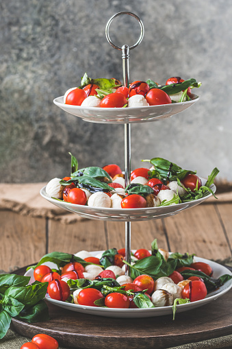 Classic italian salad Insalata Caprese with cherry tomatoes, mini mozarella pearls, basil leaves and balsamic glaze served on a cake stand, vertical
