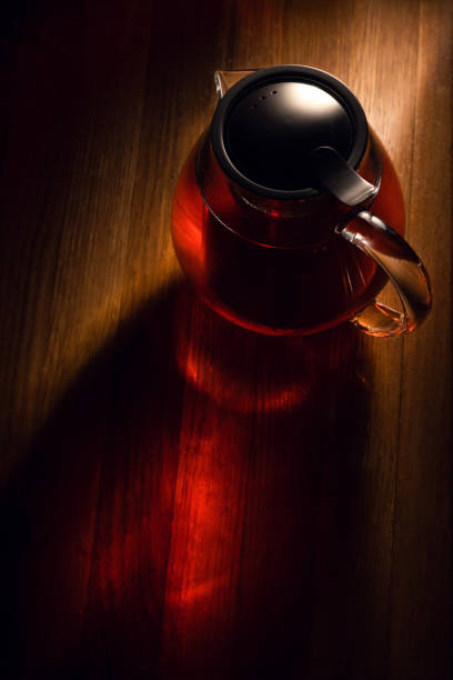 A warm-hued teapot on a wooden surface, steeping  tea, casting reflections and shadows stock photo