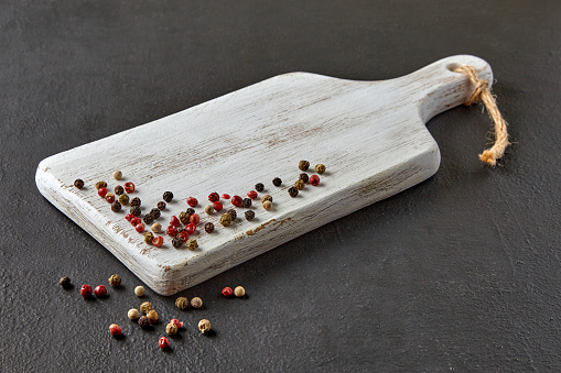 Wooden white cutting board with scattered colorful peppercorns on a black concrete countertop.