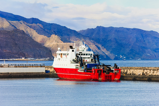 Red cargo ship in port of Santa Cruz de Tenerife, mountains in background.