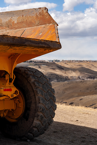 Close-up of the back of a large yellow John Deere 250 C Off Highway, Articulated Dump Truck bucket and tires, sitting near the Lethbridge Coulees.