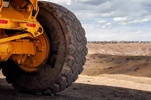 Close-up of a tire and axle of a large yellow John Deere 250 C Off Highway, Articulated Dump Truck, sitting near the Lethbridge Coulees.