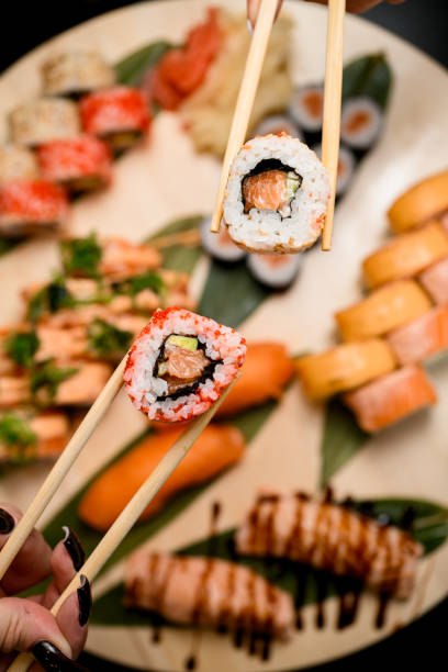 istock Female hands holding sushi rolls with chopsticks close up 2073723738