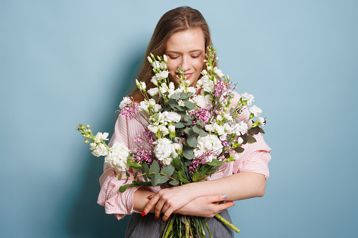 close-up portrait of a woman with a bouquet of flowers on a clean blue background, congratulations concept
