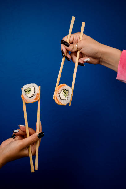istock Women's hands hold sushi rolls with chopsticks on dark blue background 2073732509