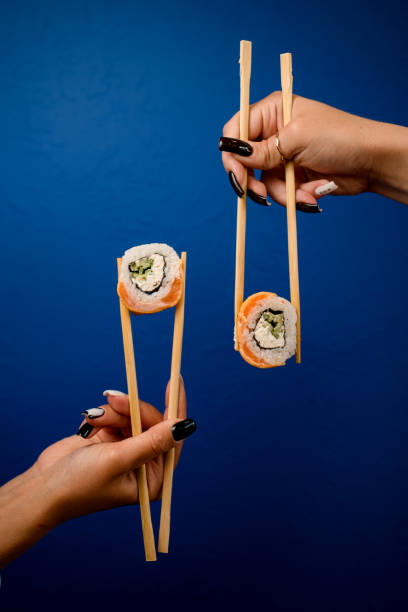 istock Female hands hold vertical sushi rolls with chopsticks on a blue background 2073733024