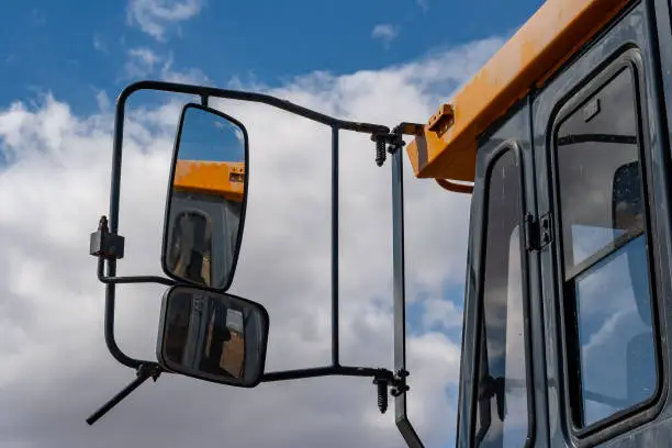 Photo of Close up of cab, side door and dual side mirrors on a yellow John Deere construction vehicle