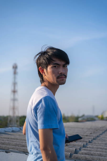 istock A dark-faced young man stands on a rooftop against a blue background. 2073750983