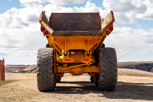 Large yellow John Deere 250 C Off Highway, Articulated Dump Truck shown from the back, sitting near the Lethbridge Coulees.  Snow fence to the left.