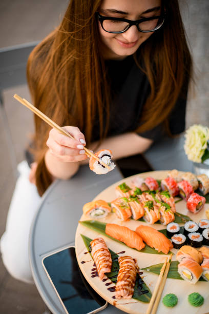 Pretty young woman with a charming smile holding a sushi roll with chopsticks