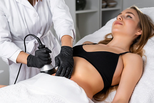 Young woman undergoes an ultrasound cavitation procedure for skin tightening.